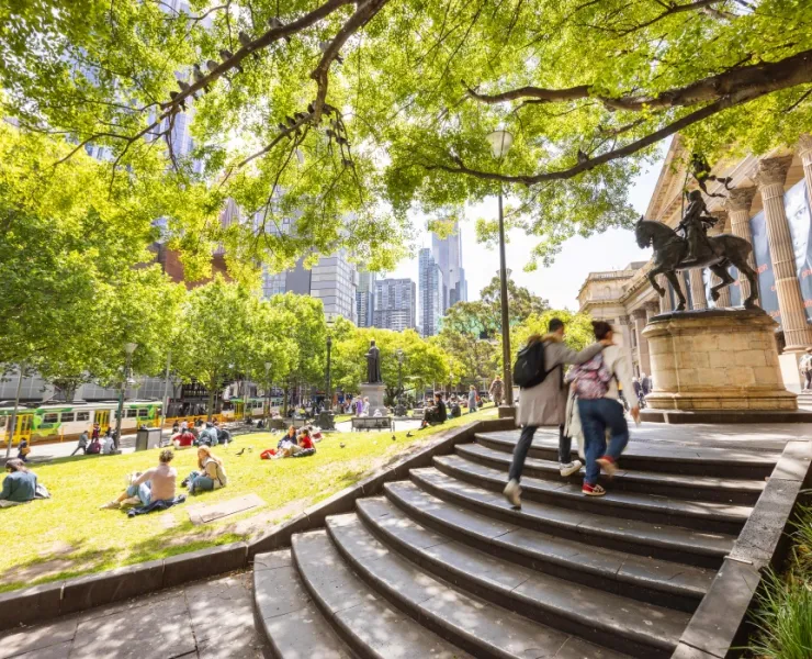 Two people going up State Library Victoria entrance stairs and statue
